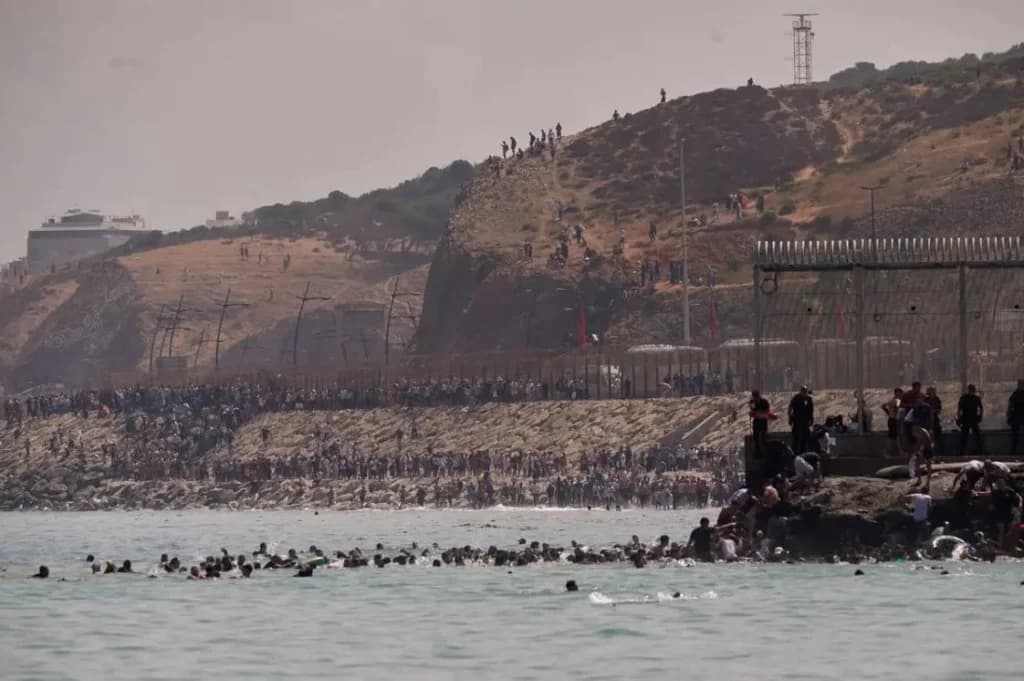 Migrantes nadando en el mar y otros en la costa de Ceuta, mientras la frontera con Marruecos está abarrotada de personas.