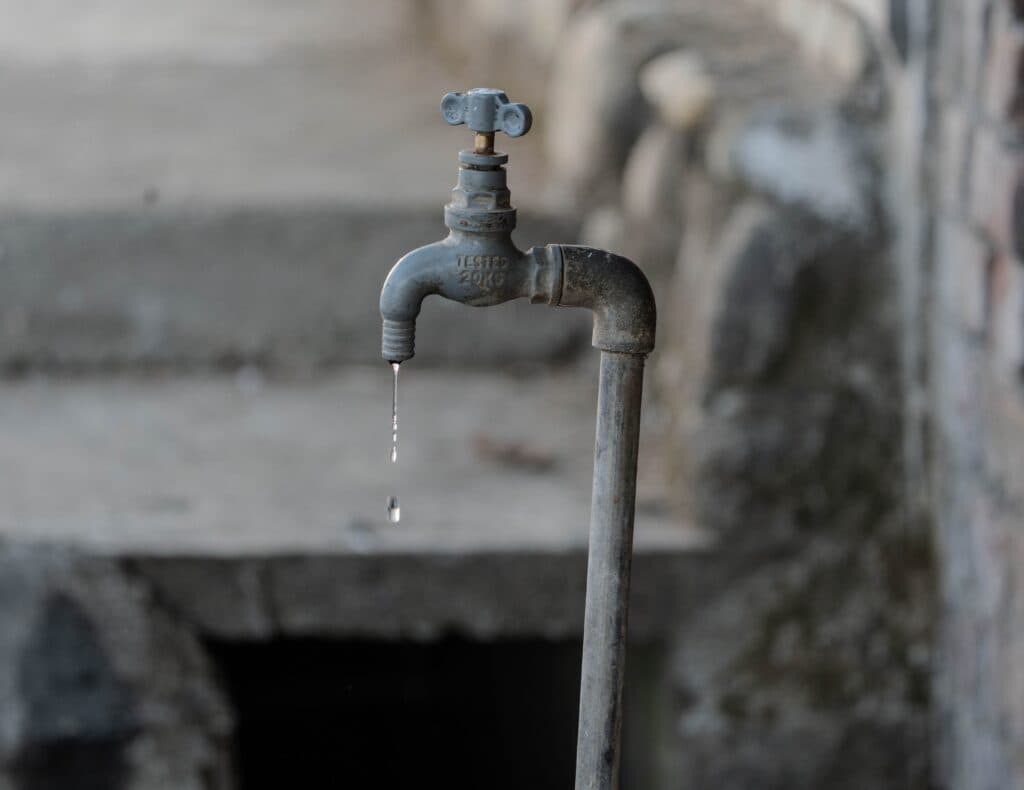 Grifo oxidado goteando agua en un entorno urbano, simbolizando la crisis de agua en CDMX por cortes programados.