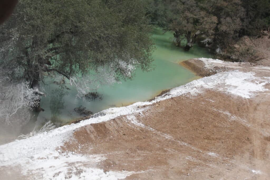Contaminación visible en el Río Sonora, con aguas turquesas y sedimentos en la orilla, reflejando el impacto del derrame de Grupo México.
