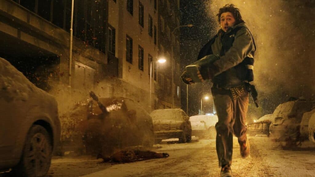 Un personaje corre por una calle nevada en medio de un caos, mientras explosiones iluminan la escena, reflejando la tensión de Resident Evil.