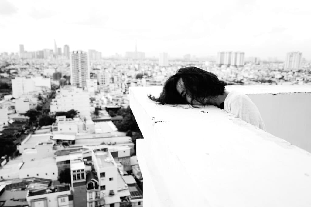 Joven con la cabeza agachada sobre un balcón, con una vista panorámica de la ciudad, reflejando la crisis de suicidios en México.